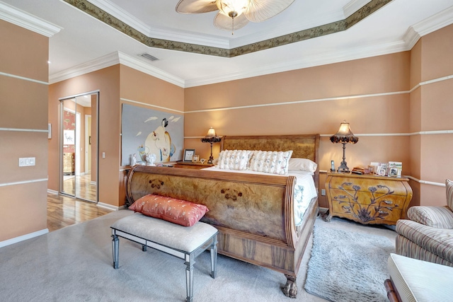 bedroom featuring a closet, crown molding, light wood-type flooring, a raised ceiling, and ceiling fan