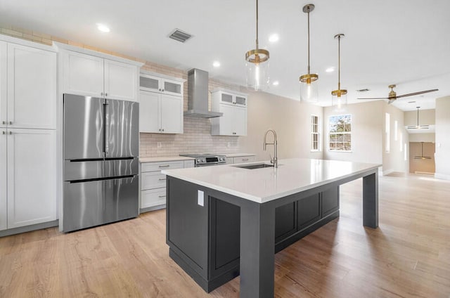 kitchen featuring appliances with stainless steel finishes, sink, an island with sink, white cabinetry, and wall chimney exhaust hood