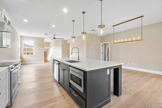 kitchen featuring hanging light fixtures, a center island with sink, sink, white cabinets, and appliances with stainless steel finishes