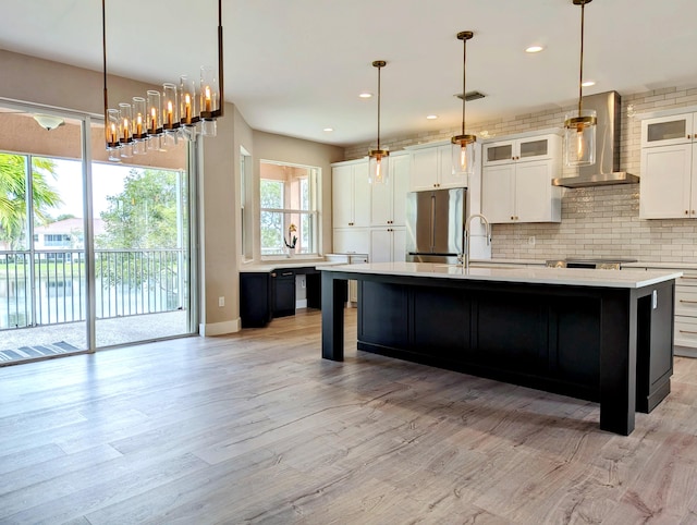 kitchen featuring high end refrigerator, wall chimney exhaust hood, a center island with sink, pendant lighting, and light hardwood / wood-style floors