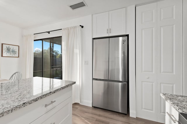 kitchen featuring light stone countertops, white cabinetry, stainless steel refrigerator, and light hardwood / wood-style floors