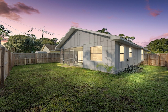 back house at dusk featuring a sunroom and a lawn