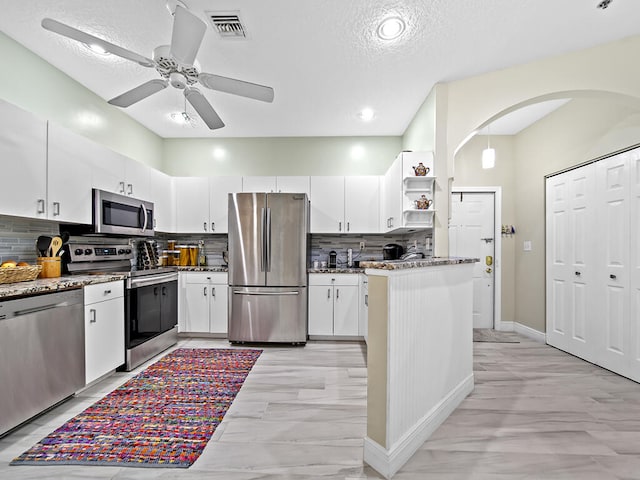 kitchen with tasteful backsplash, appliances with stainless steel finishes, a textured ceiling, white cabinetry, and light stone counters