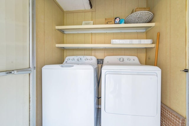 clothes washing area with washer and clothes dryer and wooden walls