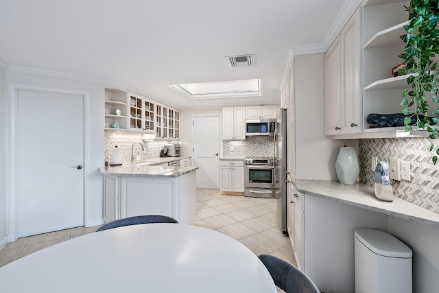 kitchen with white cabinets, light tile patterned floors, appliances with stainless steel finishes, tasteful backsplash, and kitchen peninsula