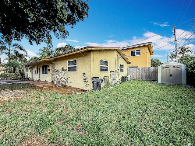 back of house with central air condition unit, a yard, and a shed