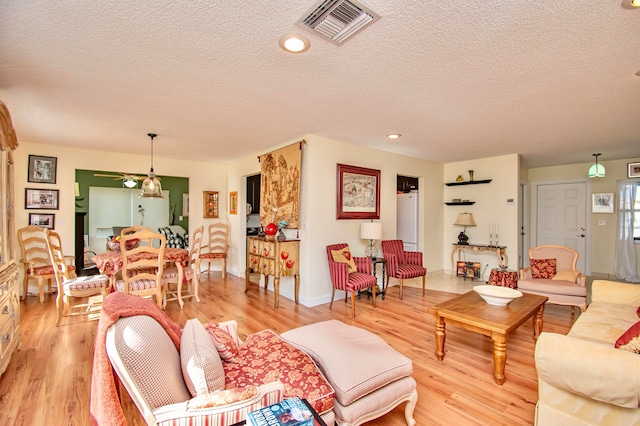 living room with light hardwood / wood-style floors, a textured ceiling, and ceiling fan