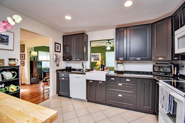 kitchen with sink, a textured ceiling, dark brown cabinets, and white appliances