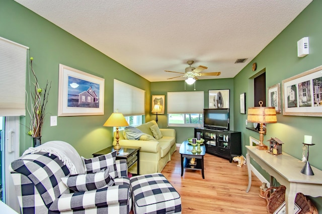 living room featuring a textured ceiling, light wood-type flooring, and ceiling fan