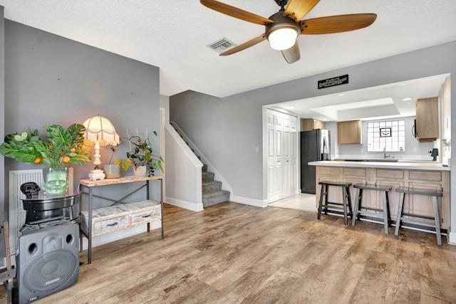 kitchen with stainless steel fridge, a textured ceiling, light hardwood / wood-style floors, a breakfast bar area, and ceiling fan