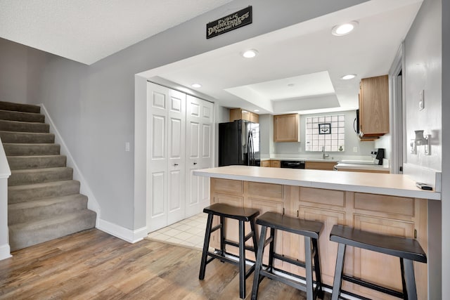 kitchen featuring a kitchen bar, light hardwood / wood-style floors, kitchen peninsula, black appliances, and sink