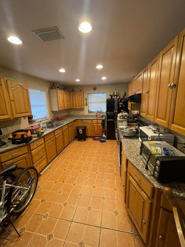 kitchen featuring black refrigerator with ice dispenser, dark stone counters, sink, stainless steel range with electric cooktop, and light tile patterned floors