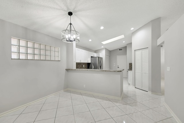 kitchen featuring kitchen peninsula, stainless steel fridge, vaulted ceiling with skylight, pendant lighting, and white cabinetry