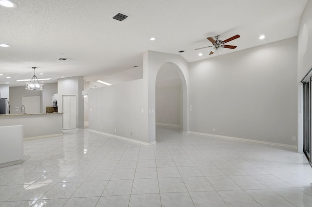 unfurnished living room with lofted ceiling, light tile patterned floors, and ceiling fan with notable chandelier