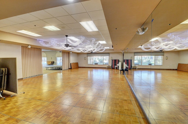 exercise area featuring a paneled ceiling, light parquet floors, and a healthy amount of sunlight