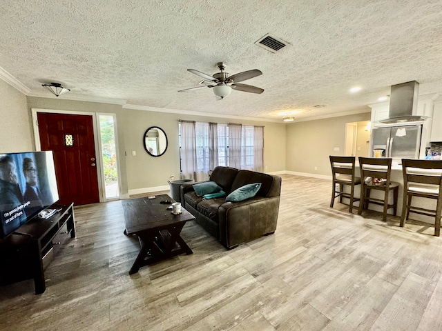 living room with ceiling fan, a textured ceiling, ornamental molding, and light hardwood / wood-style flooring