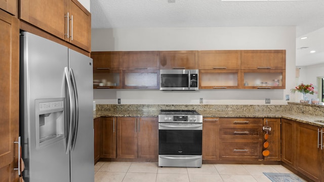 kitchen featuring stainless steel appliances, light stone countertops, light tile patterned flooring, and a textured ceiling