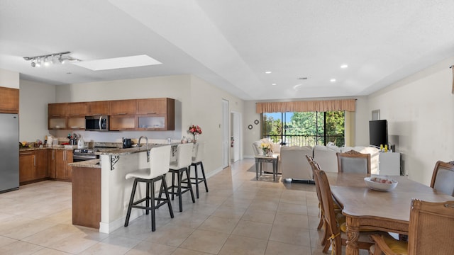 kitchen featuring a kitchen breakfast bar, kitchen peninsula, appliances with stainless steel finishes, light stone counters, and a skylight