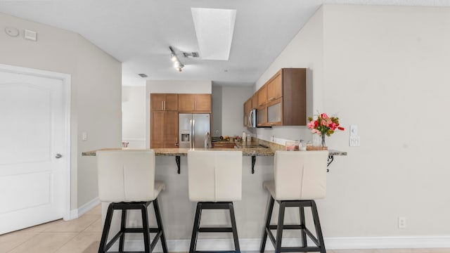 kitchen featuring a kitchen bar, a textured ceiling, kitchen peninsula, stainless steel appliances, and light tile patterned floors