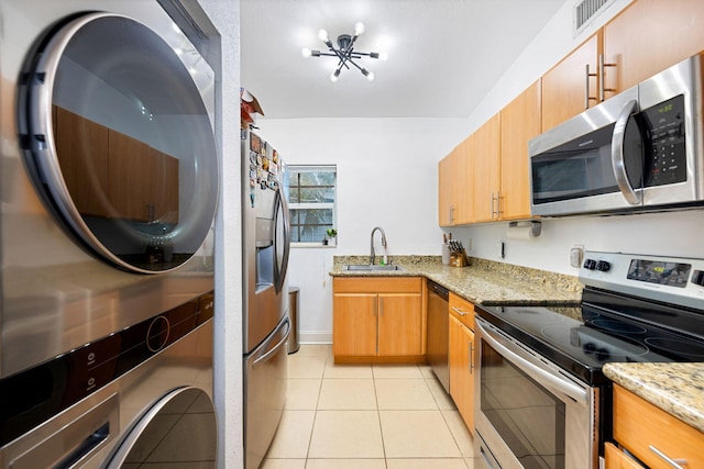 kitchen featuring light stone countertops, sink, light tile patterned floors, stacked washer and clothes dryer, and appliances with stainless steel finishes