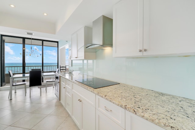 kitchen with wall chimney range hood, a chandelier, a water view, black electric stovetop, and white cabinets