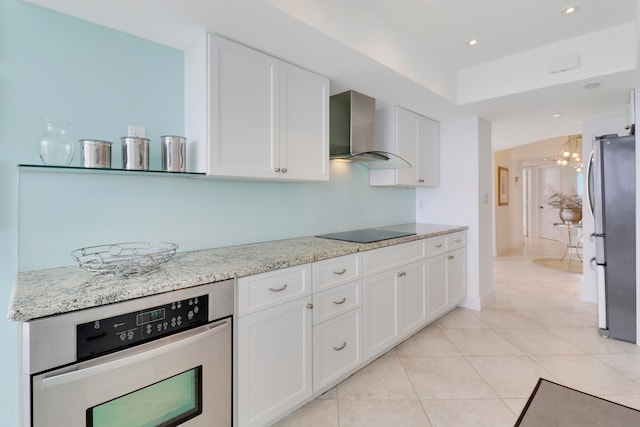 kitchen with light stone countertops, appliances with stainless steel finishes, wall chimney range hood, white cabinetry, and light tile patterned flooring