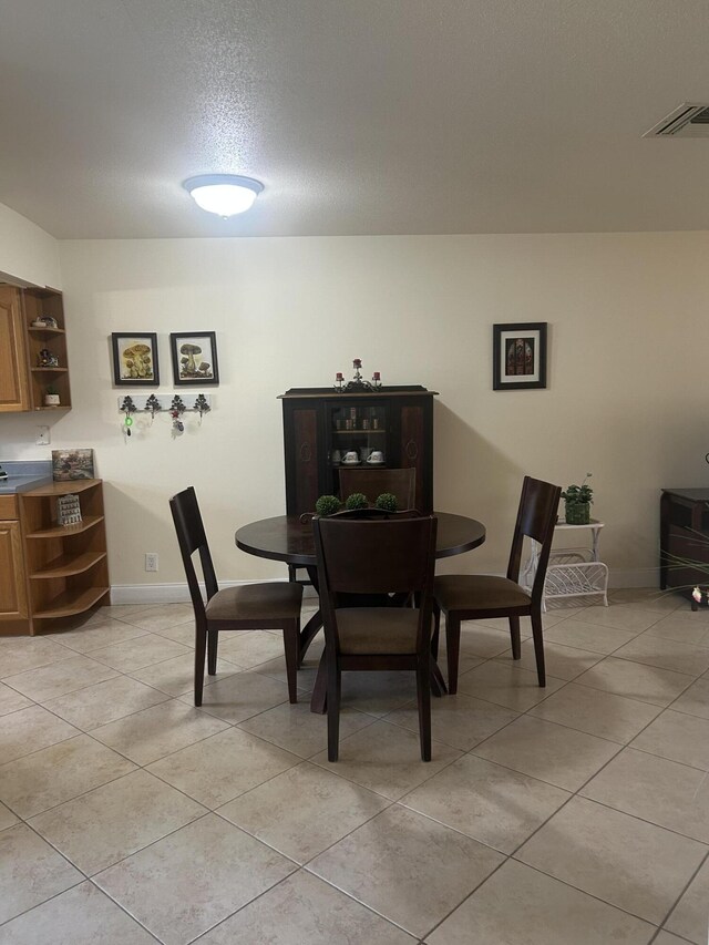 dining area featuring light tile patterned floors, visible vents, baseboards, and a textured ceiling