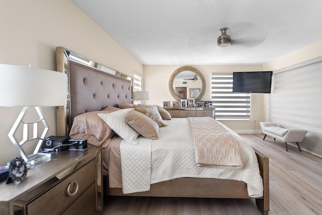 bedroom with a textured ceiling, light wood-type flooring, and ceiling fan