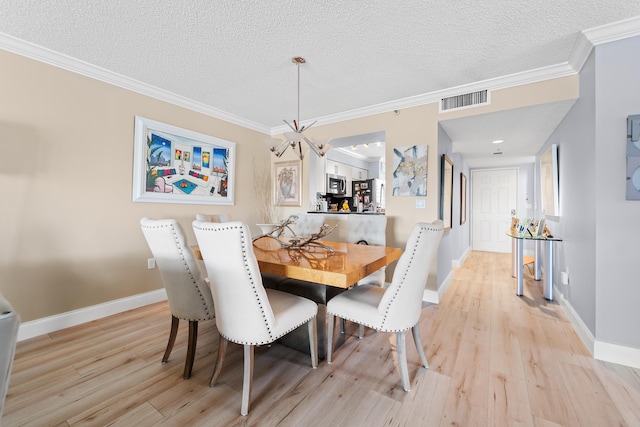 dining room with crown molding, light wood-type flooring, a textured ceiling, and an inviting chandelier