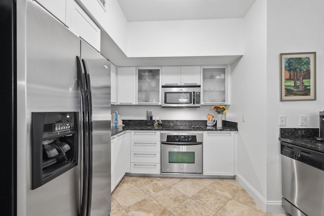 kitchen with dark stone counters, stainless steel appliances, white cabinetry, and light tile patterned floors