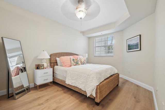 bedroom featuring ceiling fan, light hardwood / wood-style floors, and a tray ceiling