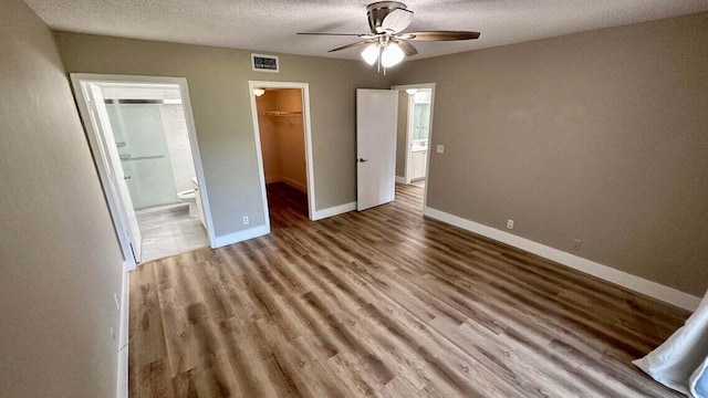 unfurnished bedroom with a spacious closet, hardwood / wood-style floors, a closet, and ceiling fan