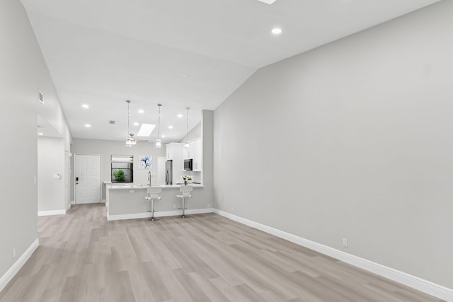 unfurnished living room with sink, light wood-type flooring, and vaulted ceiling with skylight