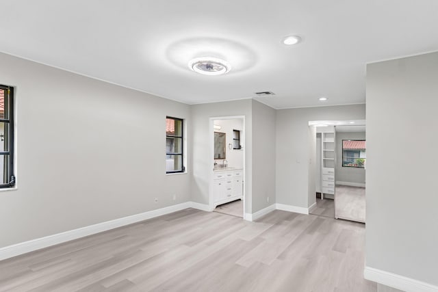 unfurnished bedroom featuring ensuite bath, light hardwood / wood-style floors, a closet, and multiple windows