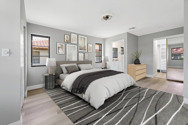 bedroom with light wood-type flooring, connected bathroom, and a closet