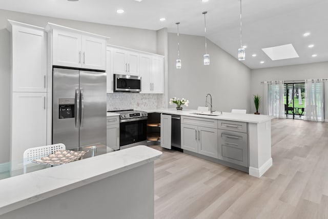 kitchen featuring hanging light fixtures, vaulted ceiling with skylight, decorative backsplash, white cabinetry, and appliances with stainless steel finishes