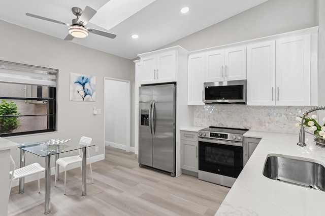 kitchen featuring stainless steel appliances, white cabinetry, lofted ceiling, decorative backsplash, and light stone countertops