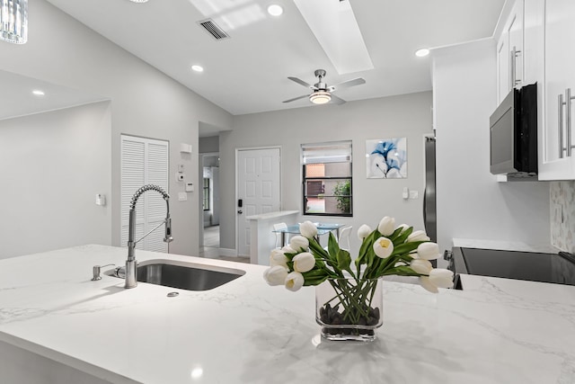 kitchen with white cabinets, vaulted ceiling, light stone countertops, ceiling fan, and sink