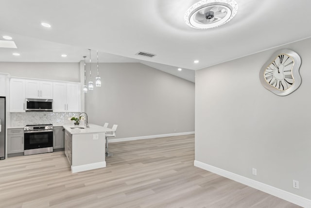 kitchen with kitchen peninsula, vaulted ceiling, pendant lighting, stainless steel appliances, and white cabinetry