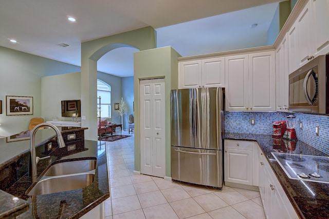 kitchen with backsplash, sink, stovetop, white cabinetry, and stainless steel refrigerator