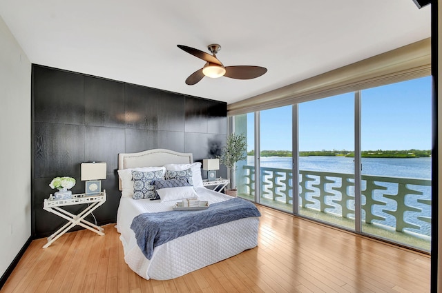 bedroom with access to outside, ceiling fan, a water view, and light wood-type flooring