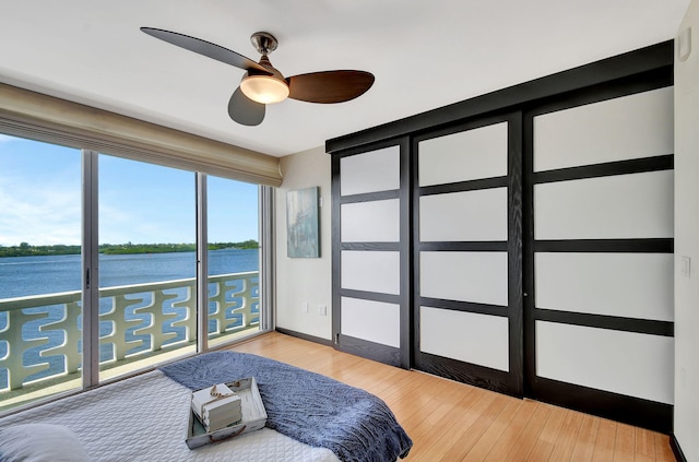 bedroom with ceiling fan, a water view, and wood-type flooring