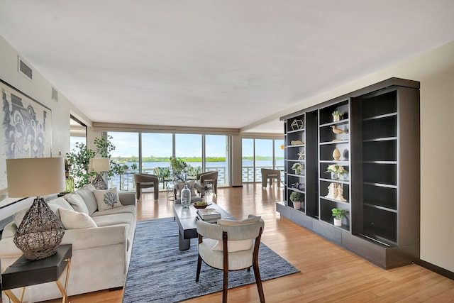 living room with light wood-type flooring, a water view, and expansive windows