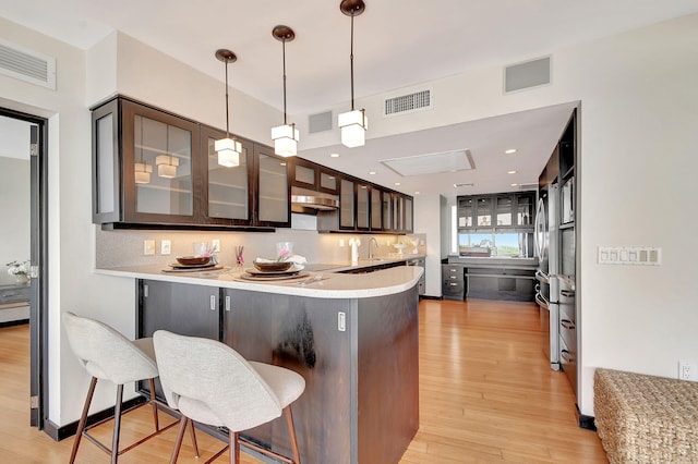 kitchen with a breakfast bar, kitchen peninsula, light wood-type flooring, decorative light fixtures, and dark brown cabinets