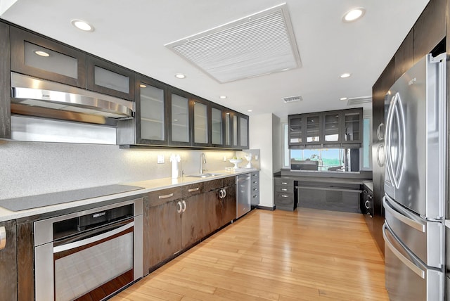 kitchen with sink, range hood, backsplash, appliances with stainless steel finishes, and light wood-type flooring