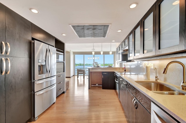 kitchen with appliances with stainless steel finishes, dark brown cabinets, sink, pendant lighting, and light hardwood / wood-style flooring