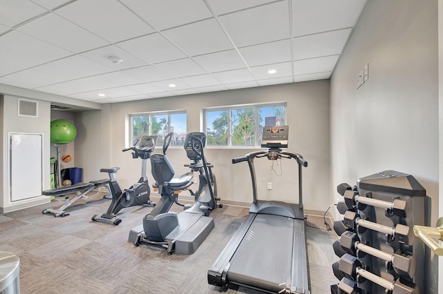 exercise room featuring a paneled ceiling and light colored carpet