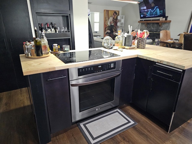 kitchen with a fireplace, oven, dark hardwood / wood-style flooring, black electric stovetop, and kitchen peninsula