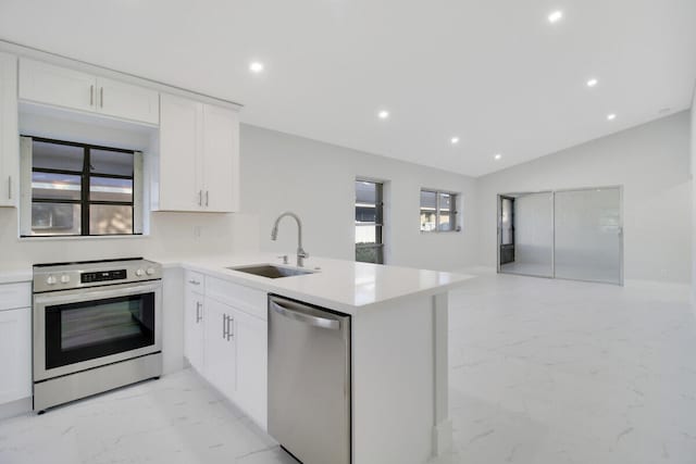 kitchen featuring lofted ceiling, kitchen peninsula, sink, appliances with stainless steel finishes, and white cabinetry