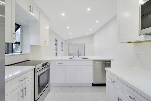 kitchen with kitchen peninsula, appliances with stainless steel finishes, vaulted ceiling, sink, and white cabinetry